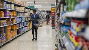 Hombre comprando en un supermercado con un presupuesto ajustado. Está buscando precios bajos debido a la inflación. Vive en el noreste de Inglaterra y utiliza su teléfono móvil para consultar su lista de la compra.