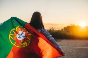 Mujer joven extendiendo la bandera portuguesa al aire libre, mientras el sol se pone.