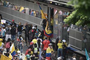 CALI, COLOMBIA - 28 DE MAYO: Miembros de primera línea de protesta evitan que una estación de autobuses sea vandalizada cuando pasan frente a la Universidad Santiago de Cali durante una manifestación contra la administración de Iván Duque el 28 de mayo de 2021 en Cali, Colombia. Las protestas contra la administración de Iván Duque no se han detenido desde que estalló el 28 de abril contra un proyecto de ley de reforma tributaria que luego fue retirado. Las demandas convirtieron su enfoque en una expresión generalizada de ira por la pobreza, la desigualdad, la mala gestión pandémica y la brutalidad policial. El gobierno nacional y el comité de huelga continúan negociando para encontrar una solución a la crisis. (Foto de Gabriel Aponte / Getty Images)