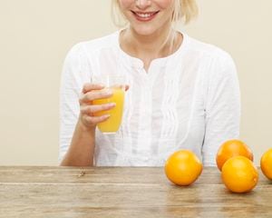 female, blonde hair, blue eyes, smile, white top, glass of orange juice, glass, oranges, biscuit background, yellow background
