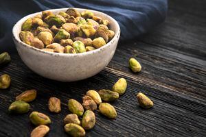 Top view of a  bowl filled with organic pistachios shot on rustic wood table.