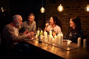 Cheerful mixed age group sitting around dining table with candles and wine, mature man talking, three friends listening and smiling, relaxation, communication, bonding, friendship