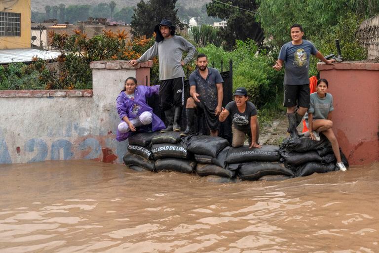 La gente mira detrás de bolsas de arena mientras el agua inunda la principal vía de acceso a Lima luego de fuertes lluvias en Chaclacayo, al este de Lima, Perú, el 15 de marzo de 2023. - Al menos 59 personas han muerto y más de 12,000 han sido afectadas por la temporada de lluvias en Perú desde septiembre por inundaciones y desborde de ríos, informó Defensa Civil el 12 de marzo de 2023. Las inundaciones acompañadas de fuertes vientos que afectan a parte de Perú aumentaron en las últimas 72 horas y afectaron zonas urbanas y rurales de los departamentos costeros de Ancash, La Libertad, Lambayeque, Piura y Tumbes, en la frontera con Ecuador. (Foto de Cris BOURONCLE / AFP)