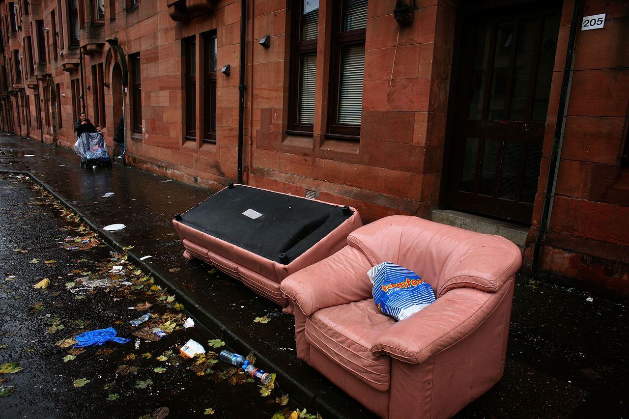 Una mujer señala algunos muebles desechados en una calle el 30 de septiembre de 2008 en el área de Govan en Glasgow, Escocia. Un informe de Campaign to End Child Poverty sugiere que millones de niños en el Reino Unido viven en hogares que sobreviven con menos de 10 libras por persona por día.