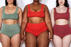 Cropped shot of a three multi-ethnic females of different sizes in lingerie on white background. Group of plus size women in lingerie standing together holding hands.