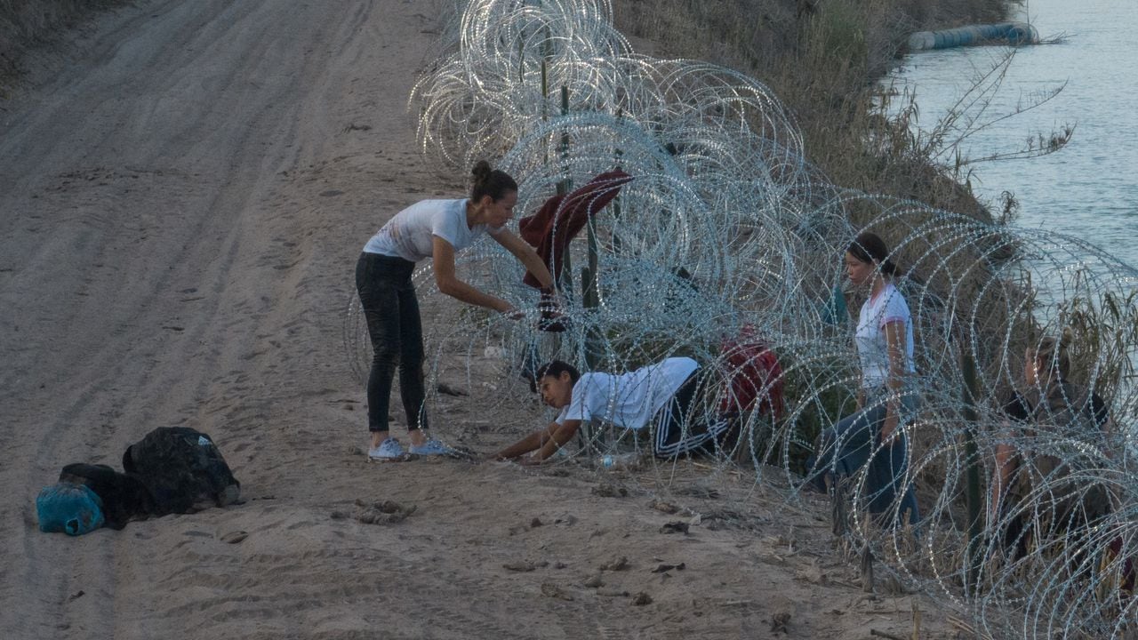 Una mujer de Colombia ayuda a sus hijos a pasar el alambre de concertina, desplegado para disuadir a los migrantes, después de que cruzaron el río Grande hacia Eagle Pass, Texas, EE. UU., el 27 de julio de 2023. REUTERS/Adrees Latif
