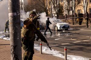 Soldados ucranianos toman posiciones en torno a una instalación militar mientras arden dos automóviles en una calle en Kiev, Ucrania, sábado 26 de febrero de 2022. (AP Foto/Emilio Morenatti)