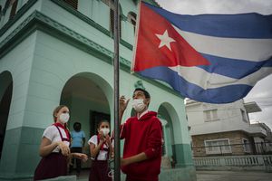 Los estudiantes que usan máscaras como medida de precaución en medio de la propagación del COVID-19 bajan la bandera cubana para que no se moje bajo la lluvia en su primer día de clases después de meses sin clases presenciales en La Habana, Cuba. Foto AP / Ramón Espinosa