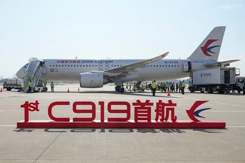 En esta imagen publicada por la agencia de noticias Xinhua, un cartel que dice "Vuelo inaugural del primer C919" se ve ante un avión de pasajeros de fabricación china, antes de su primer trayecto comercial desde Shanghái, el domingo 28 de mayo de 2023.