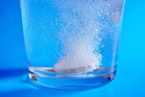 Closeup of effervescent tablet dissolving in glass of water on blue background