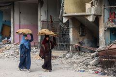 Las mujeres llevan hogazas de pan sobre sus cabezas mientras caminan frente a un edificio dañado por el bombardeo israelí en Rafah, en el sur de la Franja de Gaza, el 25 de febrero de 2024, en medio de continuas batallas entre Israel y el grupo militante palestino Hamas. (Foto de MOHAMMED ABED / AFP)