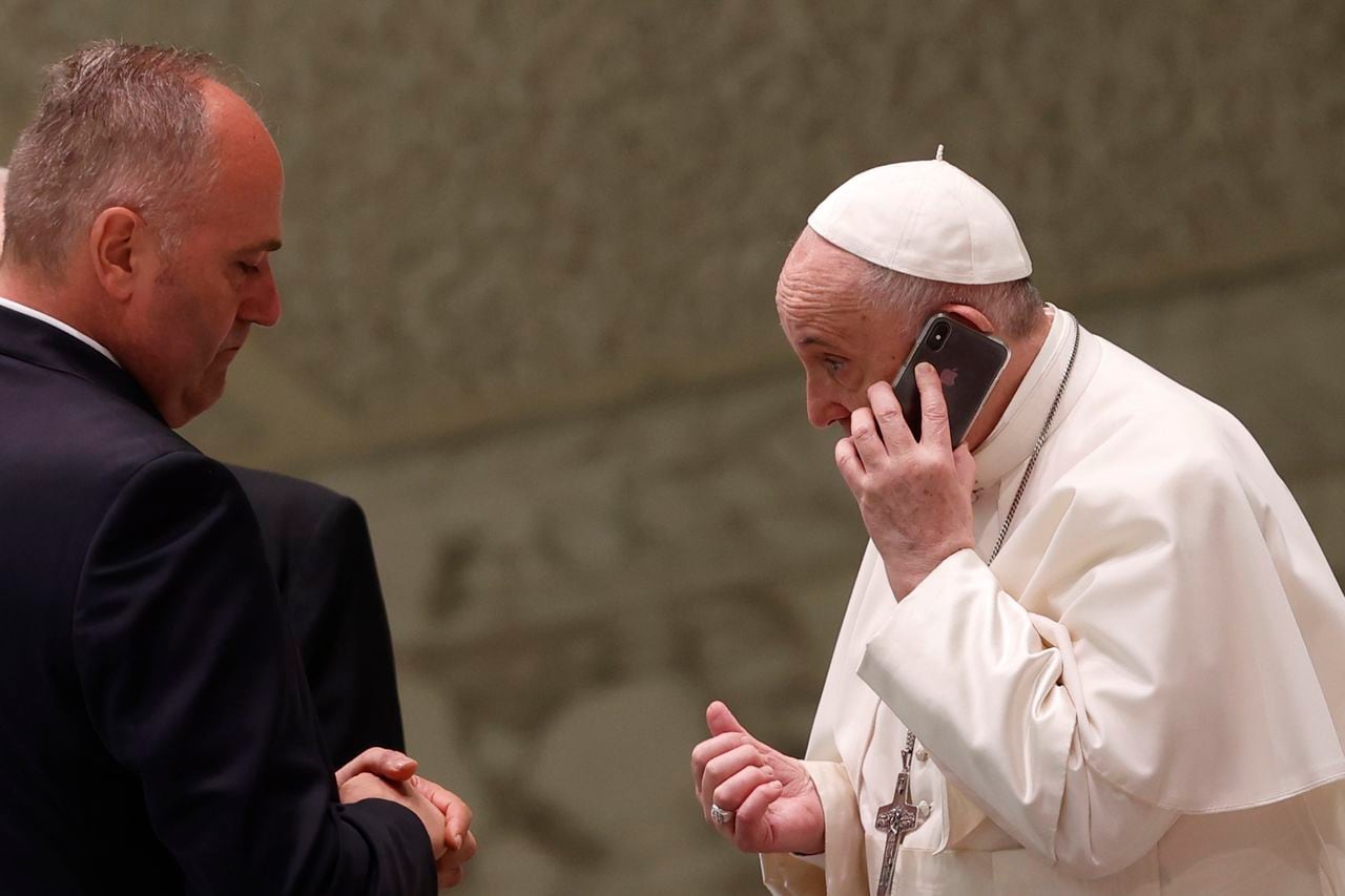 El Papa Francisco habla por teléfono, que le entregó su asistente Piergiorgio Zanetti, de pie a la izquierda, al final de su audiencia general semanal en el Salón Pablo VI del Vaticano, el miércoles 11 de agosto de 2021 (AP Photo / Riccardo De Luca)