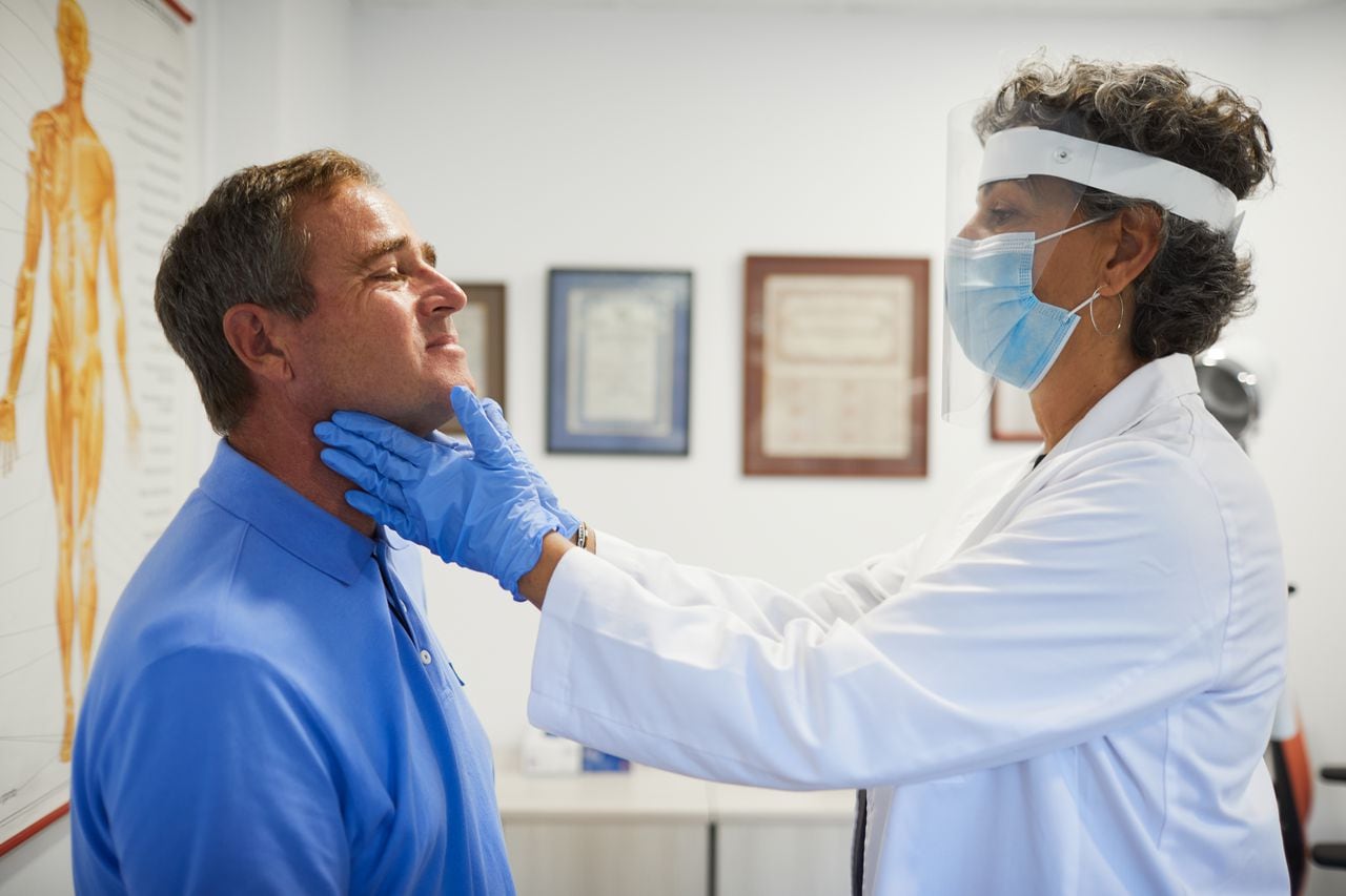 Médico endocrinólogo revisando los nódulos en el cuello de su paciente.