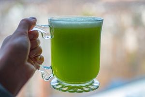 Kiwi green mix juice or smoothie in transparent mug in female hand on blurred background.