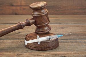 Judges Gavel And Syringe Or Injection On Brown Wooden Table Background Close-up, Front View