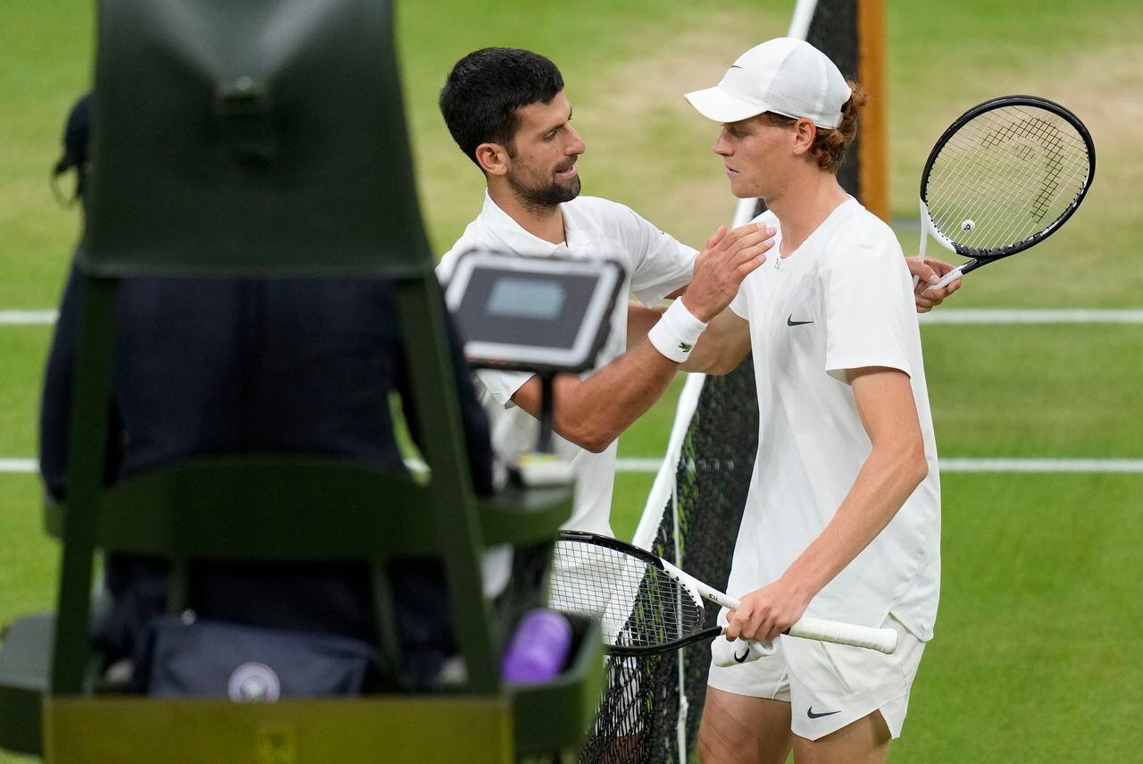 Serbia's Novak Djokovic, left, embraces Italy's Jannik Sinner after winning their men's singles semifinal match on day twelve of the Wimbledon tennis championships in London, Friday, July 14, 2023. (AP Photo/Kirsty Wigglesworth)