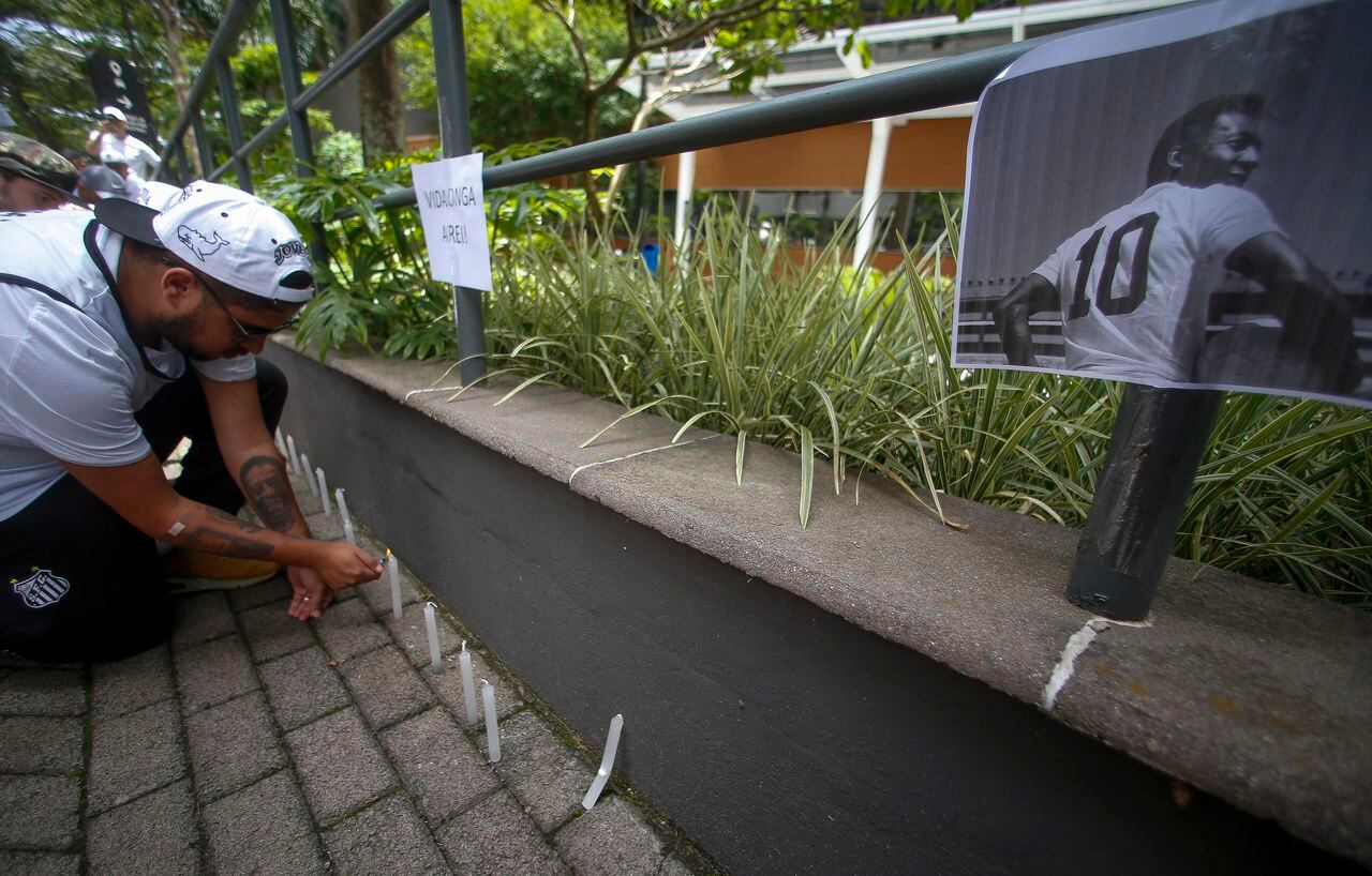 A fan of Santos lights candles next to a picture of Brazilian football legend Pele during a vigil outside the Albert Einstein Israelite Hospital entrance, where the former player is hospitalized in Sao Paulo, Brazil, on December 4, 2022. - Brazilian football legend Pele said on Saturday that he feels "strong, with a lot of hope" despite medical problems that have kept the 82-year-old sports icon in the hospital with a respiratory infection. (Photo by Miguel Schincariol / AFP)