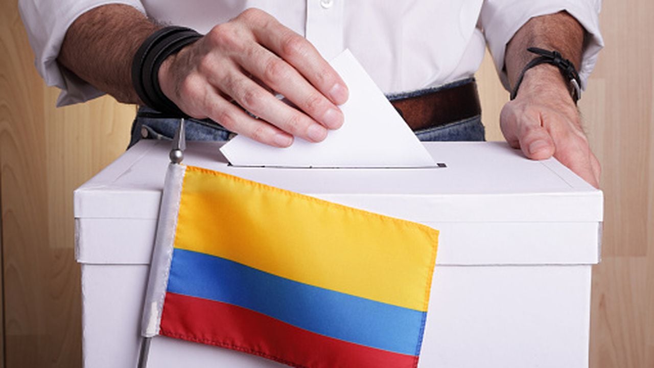 A man inserting a ballot to a ballot box.  Colombian flag in front of it.