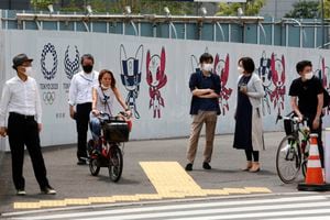 Personas se detienen en un esquina junto a un poster de promoción de los Juegos Olímpicos en Tokio el lunes 24 de mayo del 2021. (AP Photo/Koji Sasahara)