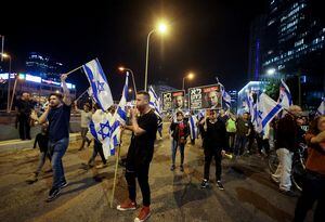 La gente sostiene banderas israelíes mientras bloquean una carretera durante una manifestación contra la reforma judicial del gobierno de coalición nacionalista de Israel