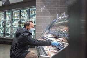 Un hombre usa mascarilla médica y guantes quirúrgicos en un esfuerzo por protegerse de contraer el coronavirus mientras compra en la tienda de comestibles