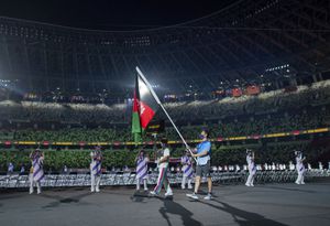 A Paralympic volunteer carries the national flag of Afghanistan during the athletes parade at the opening ceremonies for the Tokyo 2020 Paralympic Games in Tokyo, Japan, Tuesday , Aug. 24, 2021.  (Joel Marklund for OIS via AP)