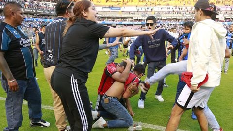 Hinchas de Atlas se cubren de los golpes en el césped del Estadio Corregidora, casa del Querétaro, en México