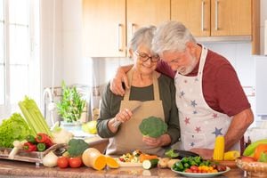 Vegetarian lifestyle. Beautiful smiling senior couple white-haired hug in the kitchen preparing a vegetable soup. On the table a mix of raw seasonal vegetables and a broccoli in the hand