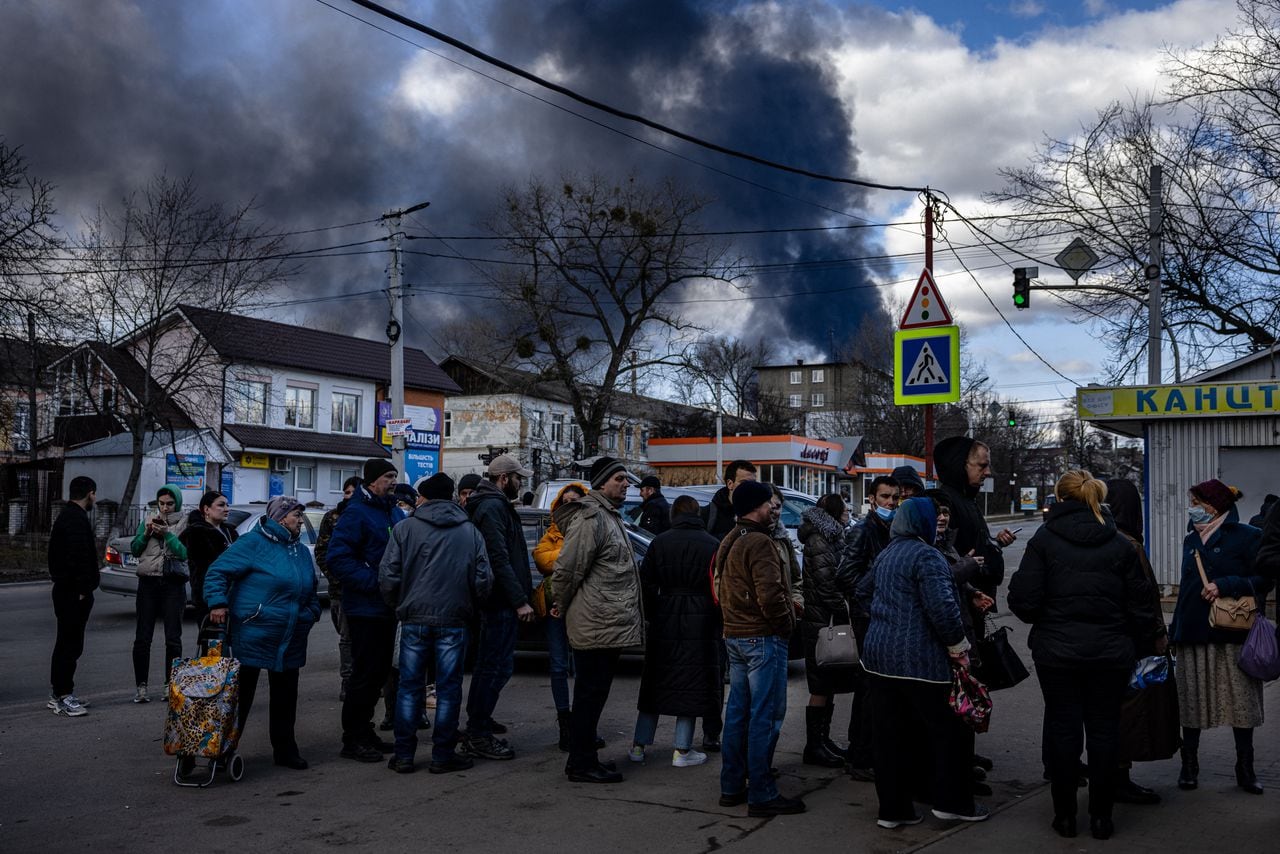 La gente hace fila frente a un supermercado mientras el humo se eleva sobre la ciudad de Vasylkiv, en las afueras de Kiev, el 27 de febrero de 2022, después de que los ataques rusos durante la noche golpearan un depósito de petróleo.  (Foto de Dimitar DILKOFF / AFP)