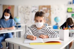 Retrato de vista frontal de un niña con tapabocas en la escuela después de la cuarentena y encierro del covid-19, escribiendo.