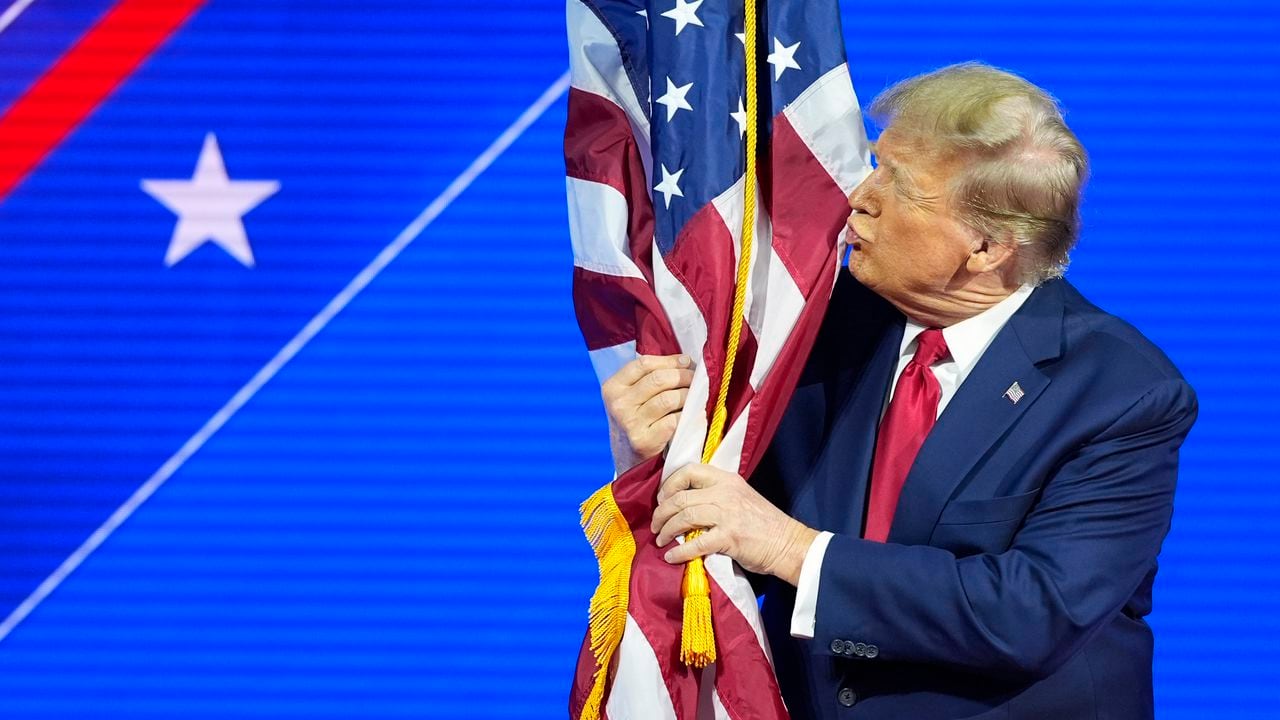 El candidato presidencial republicano, el expresidente Donald Trump, abraza y besa la bandera estadounidense mientras habla en la Conferencia de Acción Política Conservadora, CPAC.