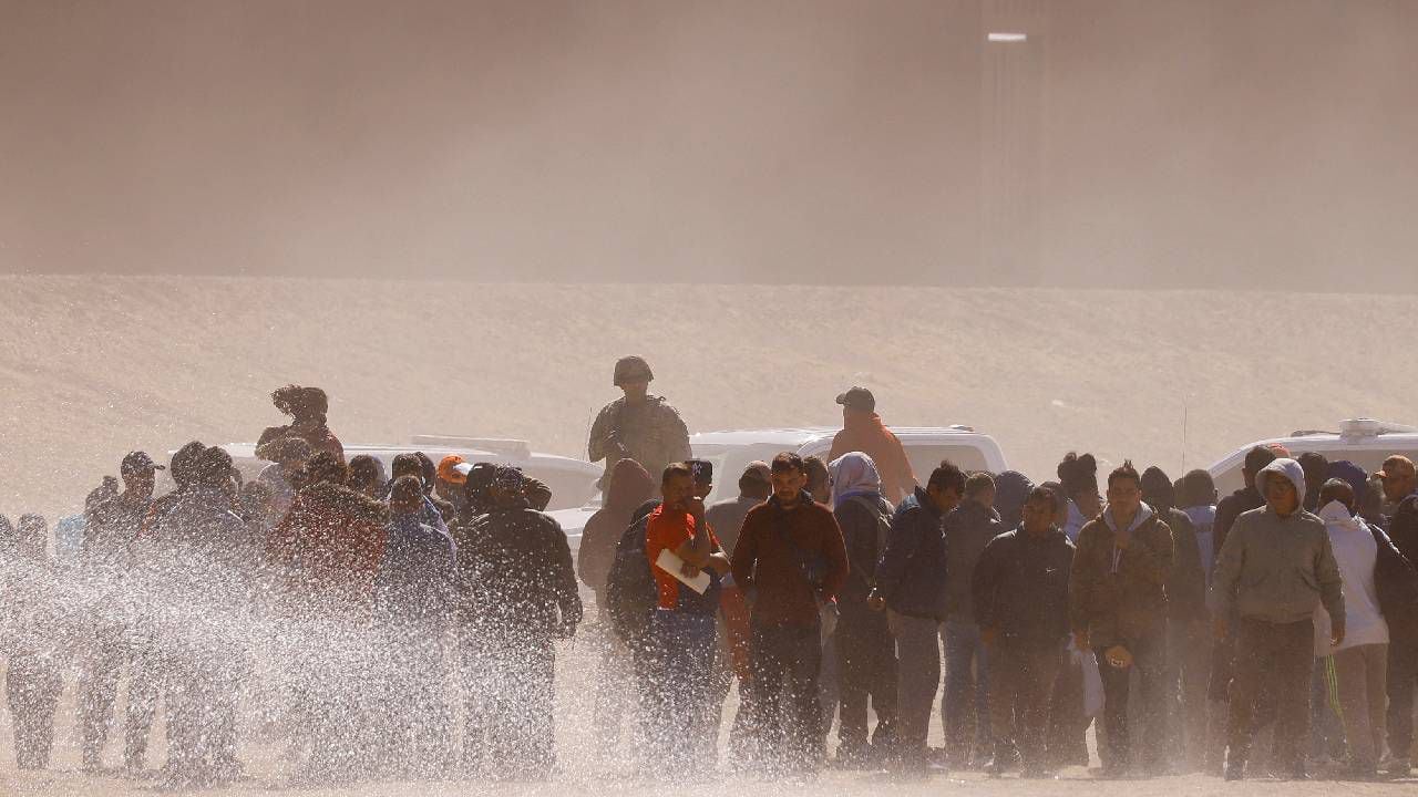 Los migrantes se paran cerca del muro fronterizo después de cruzar el río Bravo con la intención de entregarse a los agentes de la Patrulla Fronteriza de los Estados Unidos.