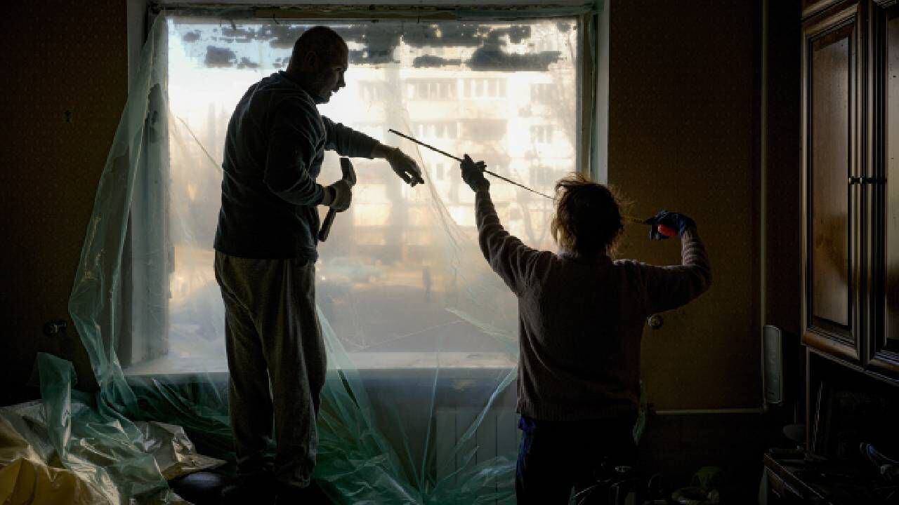 Slava Chikov, a la izquierda, cubre la ventana reventada de su salón con un plástico, en edificio dañado por una bomba el día anterior, en Kiev, Ucrania, el lunes 21 de marzo de 2022. Imagen de referencia. Foto: AP Foto/Vadim Ghirda.