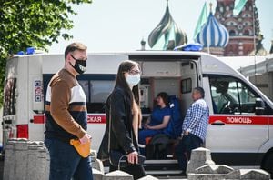 People wearing face masks walk along Red Square in front of St. Basil's cathedral in central passing an ambulance Moscow on June 18, 2021, amid the crisis linked with the Covid-19 pandemic caused by the novel coronavirus. - Moscow hits a new record confirmed 9,056 new Covid-19 daily cases as apart of 17,262 cases in Russia overall. (Photo by Alexander NEMENOV / AFP)