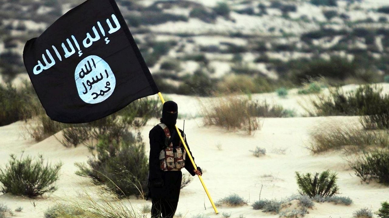 Un soldado enmascarado del Estado Islámico posa sosteniendo la pancarta de ISIL en algún lugar de los desiertos de Irak o Siria.