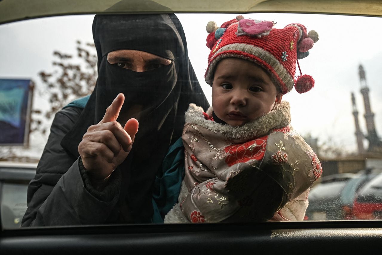Una mujer carga a un niño mientras mendiga a los viajeros en un automóvil en Kabul el 26 de diciembre de 2021. (Foto de Mohd RASFAN / AFP)