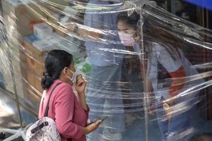 Un cliente que usa una máscara protectora para ayudar a frenar la propagación del coronavirus ordena medicamentos a través de láminas de plástico frente a una farmacia en Bangkok, Tailandia, el jueves 27 de mayo de 2021 (AP Photo / Sakchai Lalit).