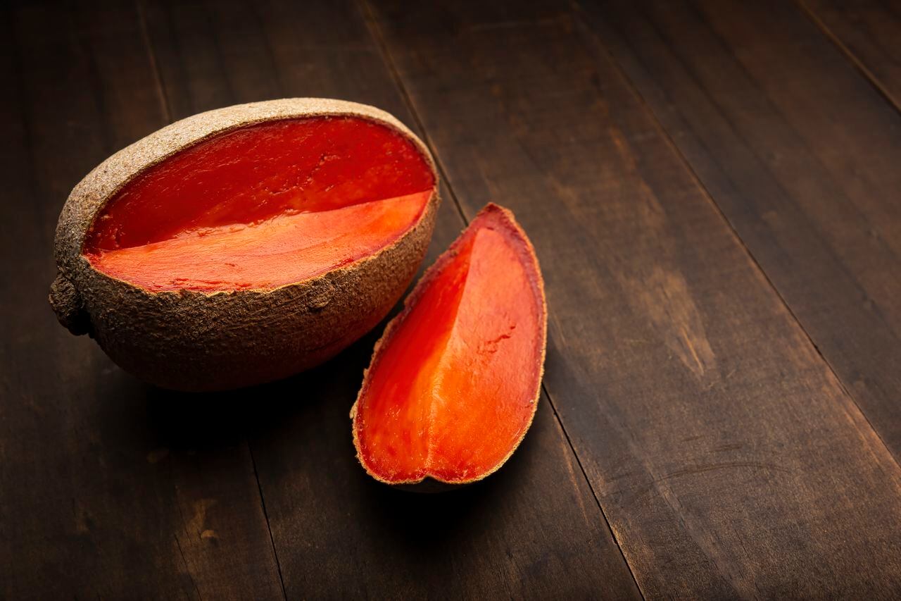 still life image of one mexican red mamey close up on rustic wooden surface and black background