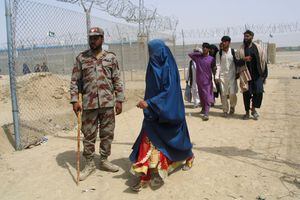 Una mujer afgana revestida en un Burqa pasa pasando el soldado paramilitar del Pakistán, ya que ella, junto con otros, ingresa a Pakistán a través de la Puerta de la Puerta de la Amistad, en la ciudad fronteriza de Pakistán y Afganistán, Pakistán, 17 de agosto de 2021. Reuters / Saeed Ali Achakzai