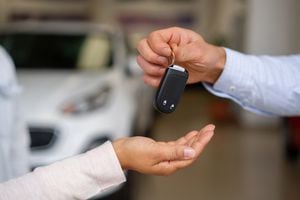 Close-up on a salesman giving the keys to their new car to a happy couple at the dealership - car ownership concepts