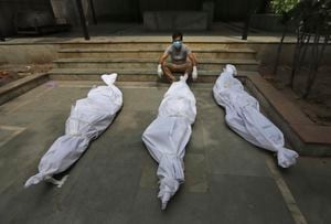 Un hombre espera para la cremación de su familiar, puesto alado de otros dos víctimas quienes murieron a causa de covid-19. New Delhi, India