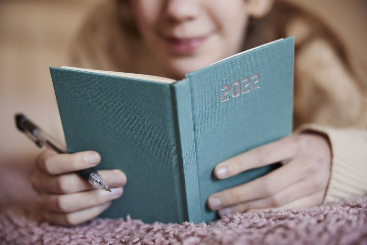 Primer plano de una adolescente acostada en la cama escribiendo en un diario de 2022