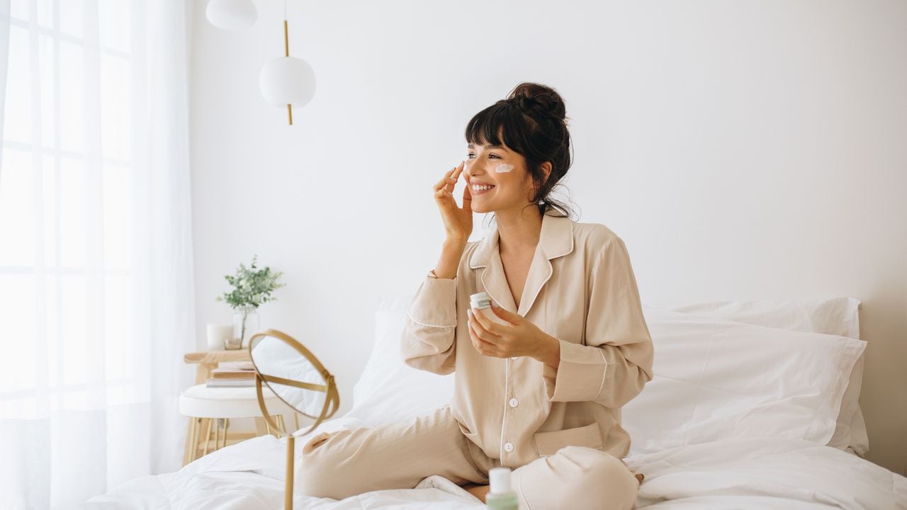 Mujer sonriente aplicar crema facial sentada en la cama