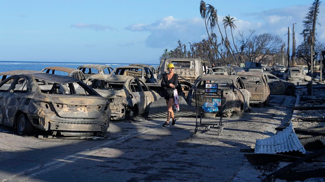 Una mujer camina entre los restos de vehículos consumidos por el fuego, el viernes 11 de agosto de 2023, en Lahaina, Hawai. (AP Foto/Rick Bowmer)