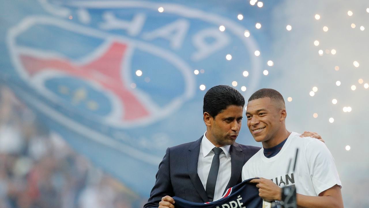PSG President Nasser Al-Khelaifi, left, speaks to PSG's Kylian Mbappe who holds a shirt with his name and 2025 on it as it is announced he has signed a three year extension to his contract on the pitch ahead of the French League One soccer match between Paris Saint Germain and Metz at the Parc des Princes stadium in Paris, France, Saturday, May 21, 2022. (AP Photo/Michel Spingler)