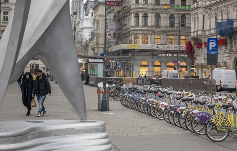 La gente pasa junto a las bicicletas de alquiler en las afueras de la Ópera Estatal, en el centro de la ciudad de Viena, que normalmente está llena de gente, en Viena, Austria, el 22 de noviembre de 2021 (Photo by JOE KLAMAR / AFP)