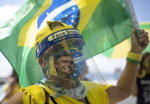 A woman wearing a face shield and mask decorated with an image of Brazilian President Jair Bolsonaro takes part in a demonstration to show support for Bolsonaro, after leaders of all three branches of the armed forces jointly resigned following the president's replacement of the defense minister, on Copacabana beach in Rio de Janeiro, Brazil, Wednesday, March 31, 2021. (AP Photo/Silvia Izquierdo)