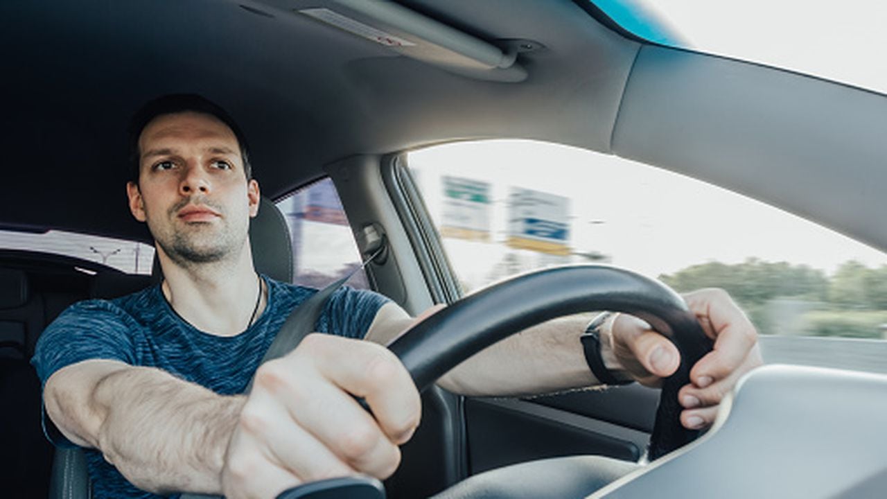 El joven conductor emocionado que sostiene un volante con las manos mira hacia adelante con curiosidad mientras conduce un automóvil a alta velocidad en la autopista. Un hombre con cinturón de seguridad en el interior de un vehículo.