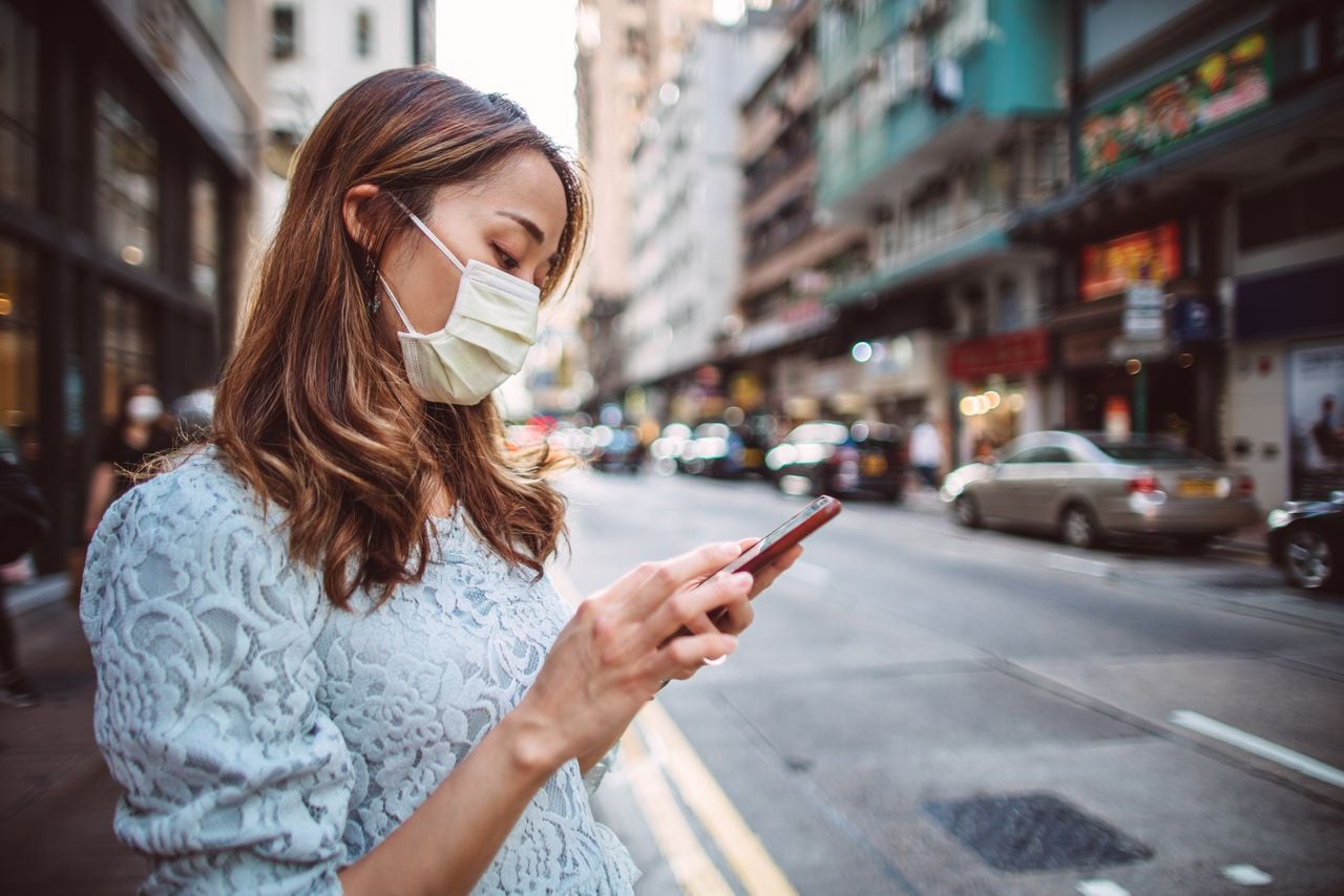 Joven bonita a mujer asiática con mascarilla médica con smartphone mientras explora en la calle de la ciudad local.