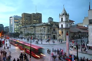 En las intersecciones de Avenida Jiménez y Carrera Séptima, los autobuses rojos de Transmilenio se detienen en la estación Museo del Oro frente a la Iglesia de San Francisco del siglo XVI, la iglesia restaurada más antigua de Bogotá.